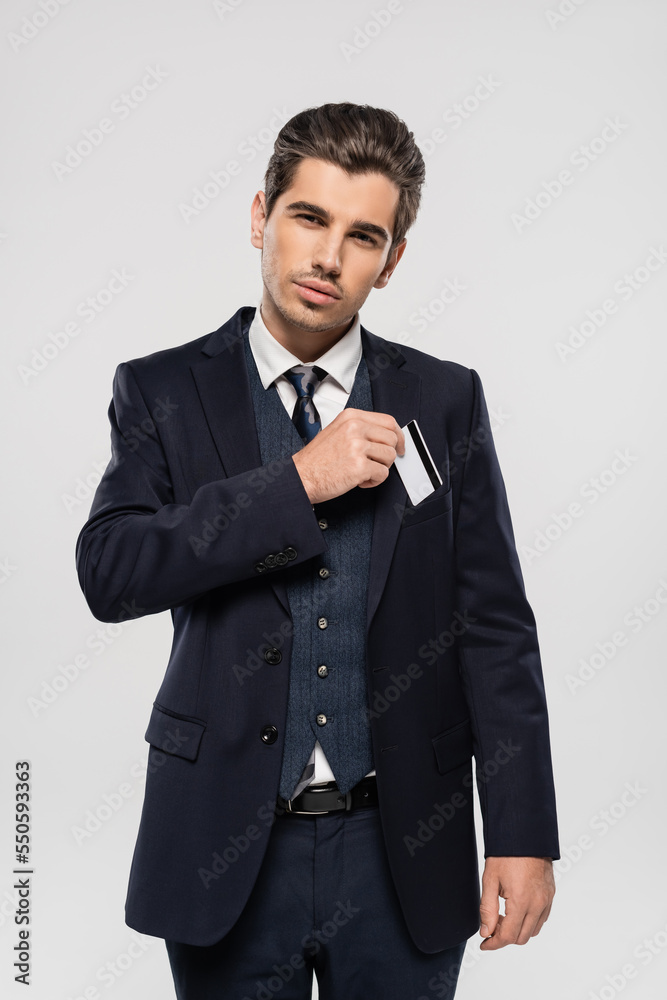 successful businessman in suit putting credit card in pocket isolated on grey successful businessman in suit putting credit card in pocket isolated on grey