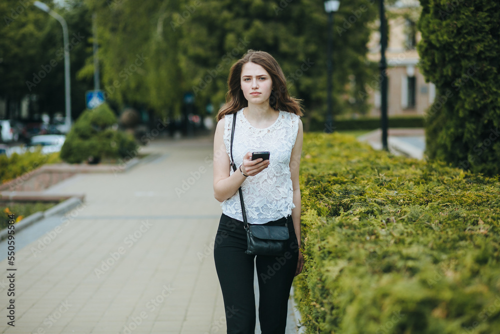 Happy beautiful young Caucasian girl with smart phone outdoors on sunny summer day texting and smiling Happy beautiful young Caucasian girl with smart phone outdoors on sunny summer day texting and smiling