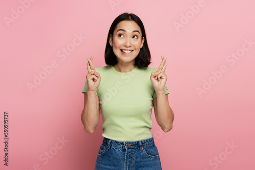 Portrait of asian woman holding crossed fingers and wishing for good luck photo