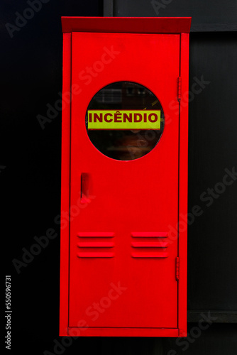 Caixa estreita de incêndio pintada de vermelho vivo com parta com visor e inscrição INCÊNDIO. photo