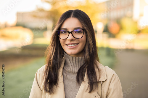Close-up portrait of independent woman student 20s with amazing smile wearing glasses in the street