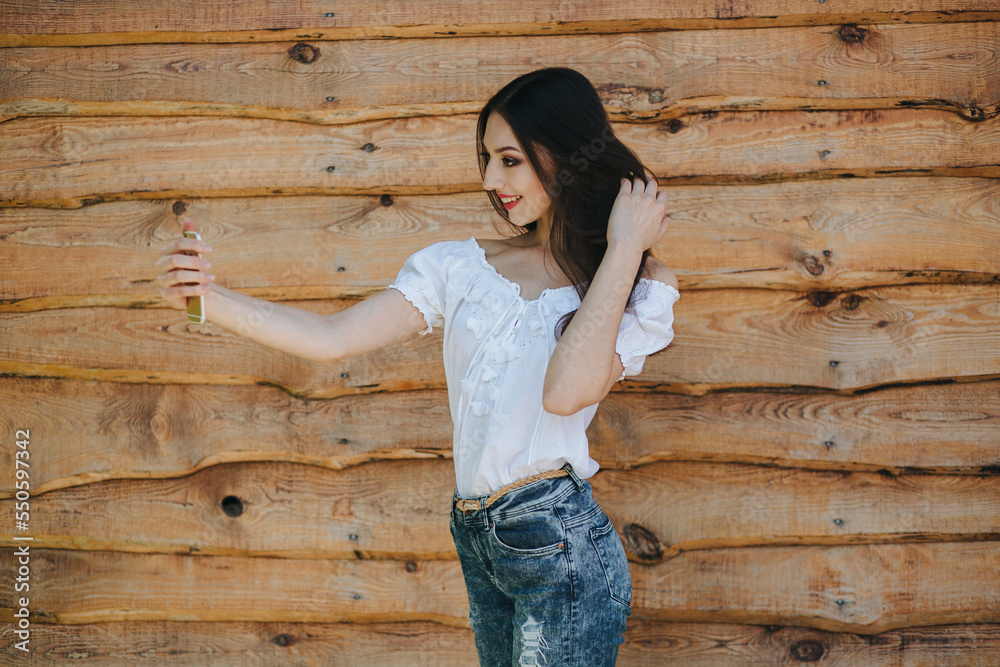 Attractive young brunette female standing with mobile phone against wooden wall background Attractive young brunette female standing with mobile phone against wooden wall background