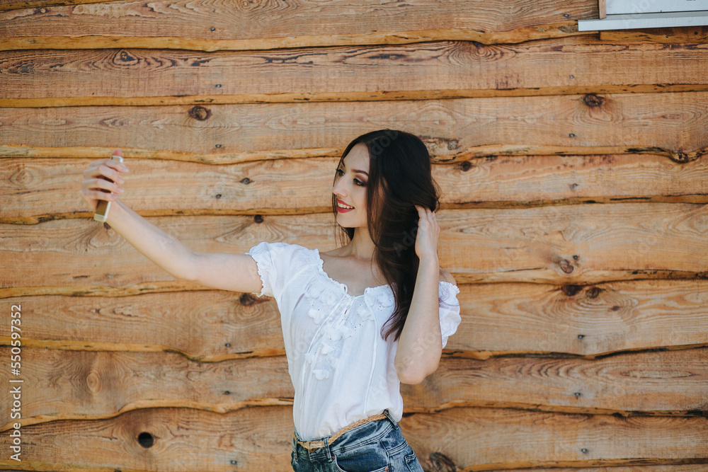 Attractive young brunette female standing with mobile phone against wooden wall background Attractive young brunette female standing with mobile phone against wooden wall background