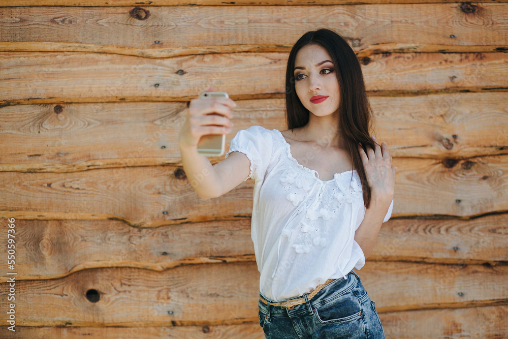 Attractive young brunette female standing with mobile phone against wooden wall background Attractive young brunette female standing with mobile phone against wooden wall background