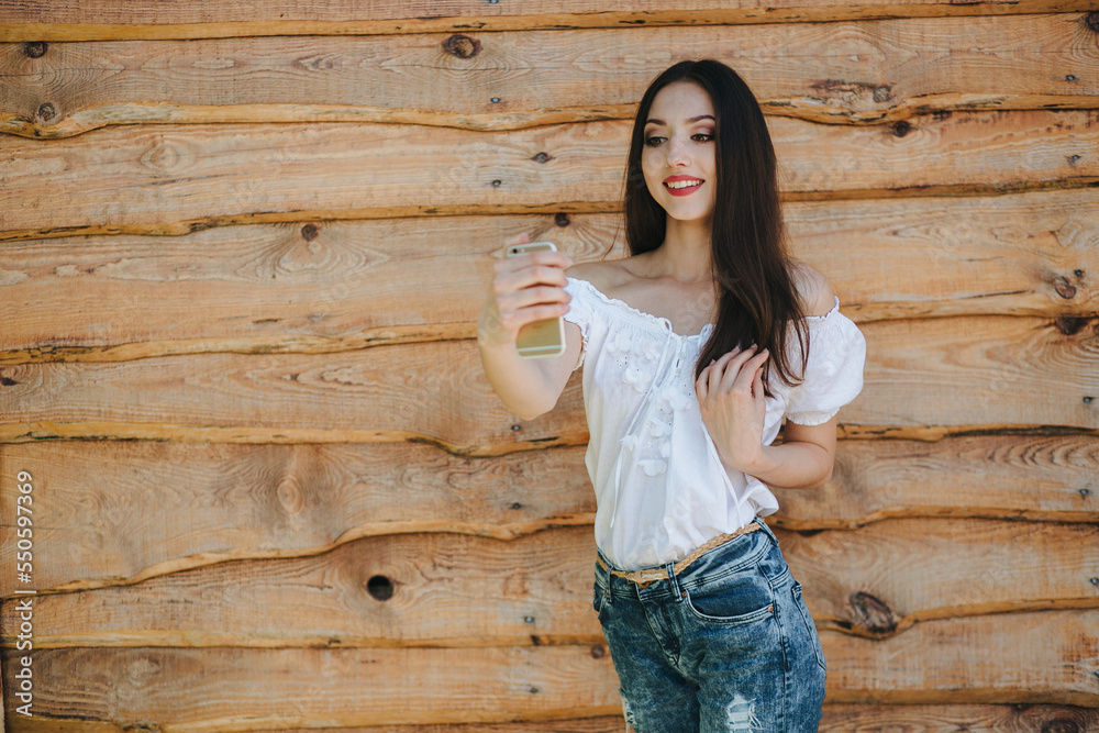 Attractive young brunette female standing with mobile phone against wooden wall background