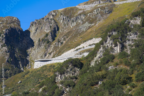 Cliff with Swiss mountain pass road in the foreground at mountain hamlet Gletsch, Canton Valais, on a sunny late summer noon. Photo taken September 12th, 2022, Gletsch, Switzerland.