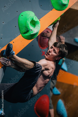 A young, athletic guy with a beautiful inflated body climbs a bouldering in a climbing hall. Emotions on the face.