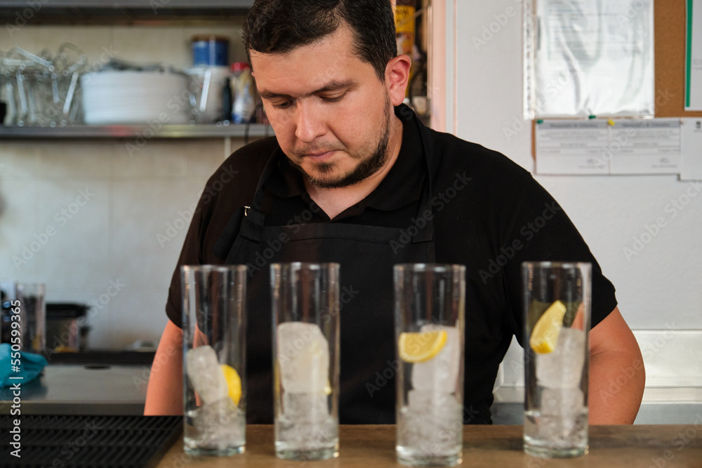 Latin man preparing soft drinks in a glasses with lemon and ice. Restaurant or bar. Latin man preparing soft drinks in a glasses with lemon and ice. Restaurant or bar.