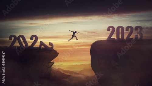 Fotografiet Determined man jump over a chasm obstacle to reach the new 2023 peak and let 2022 behind