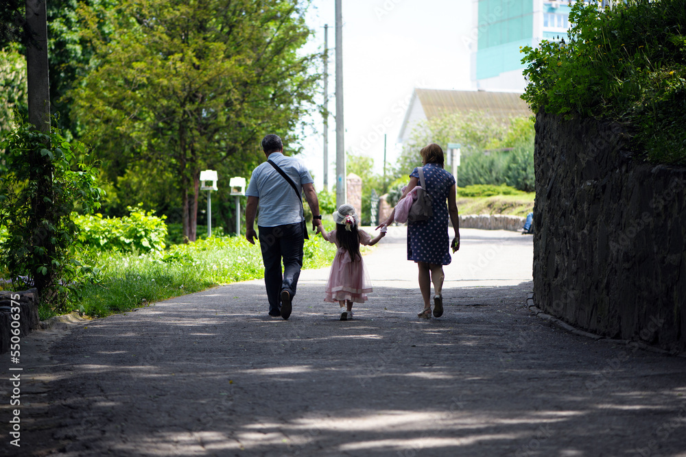 family walking in the park. mom dad and little girl walking holding hands. back view. daughter in a pink dress. friendly loving family concept, love. outdoor, walk in the fresh air, threesome