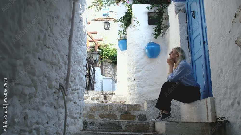 charming woman sitting by the blue door on the street with white houses charming woman sitting by the blue door on the street with white houses