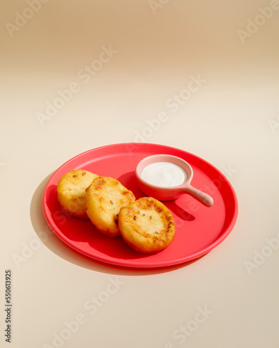 Cheese pancake with sour cream on pink plate closeup isolated on beige background