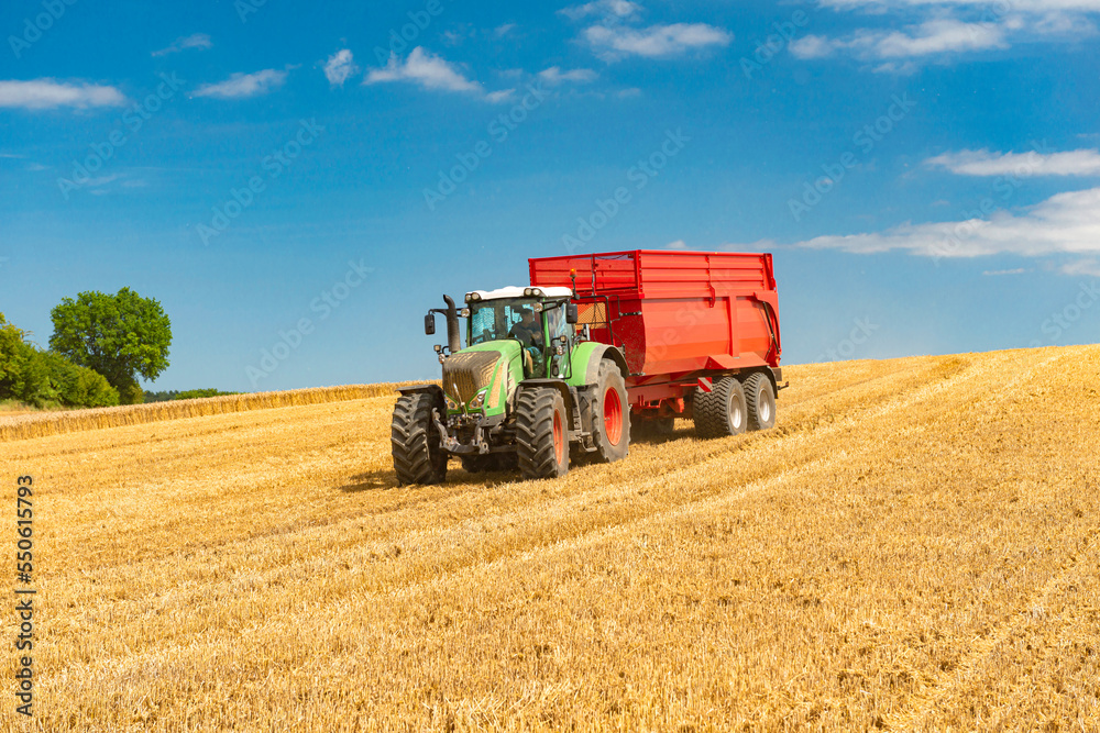 Tractor with loader wagon during grain harvest in the cornfield Tractor with loader wagon during grain harvest in the cornfield