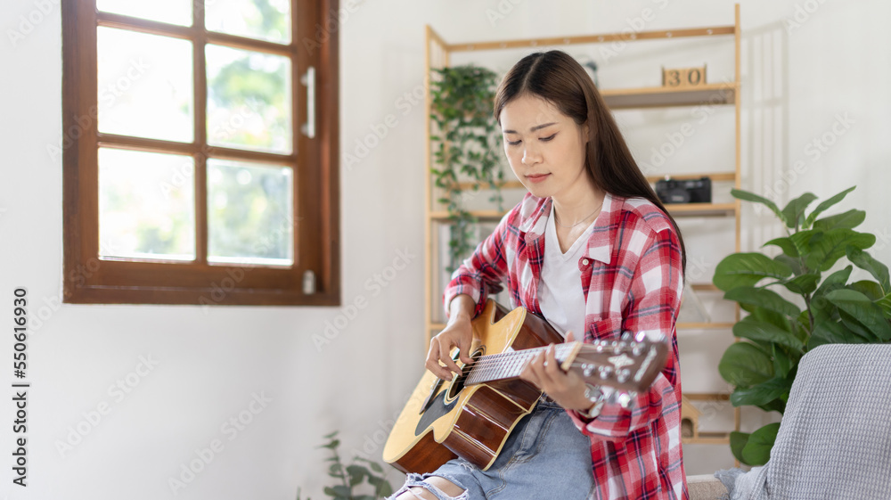 Asian female artist playing the guitar and singing happily in the living room, Relaxation with music therapy, Spending free time with music, Joy of playing music, Acoustic guitar. Asian female artist playing the guitar and singing happily in the living room, Relaxation with music therapy, Spending free time with music, Joy of playing music, Acoustic guitar.