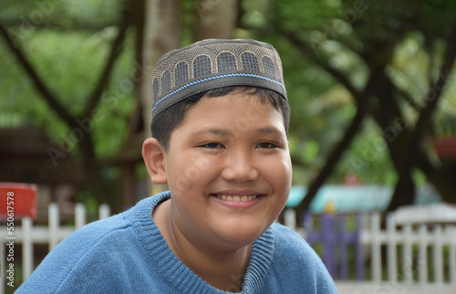 Portrait asian muslim or islamic boy sitting in the school park and smiling happily, soft and selective focus. photo