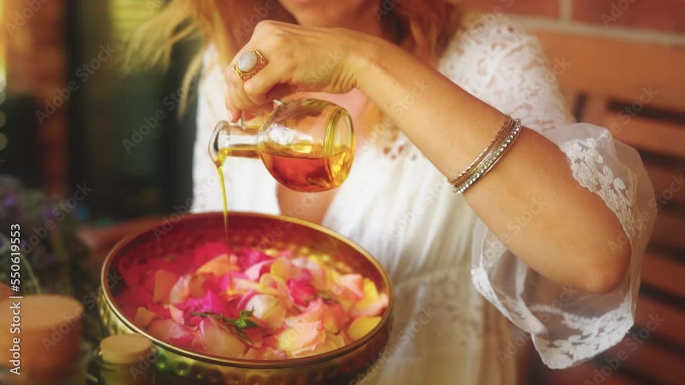 Rose flower and essential oil. Spa and aromatherapy. Woman pours essential oil into a beautiful brass bowl full of flowers.