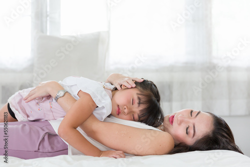 Child little girl sleep on mother's on bed at home. Mother take care her Asian daughter with kindness. family, love, happy and new life concept © amorn