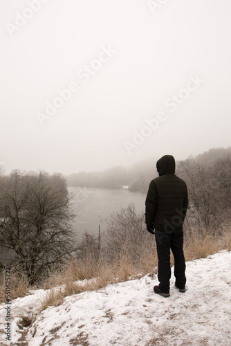 A pensive man stands on a high cliff near a river