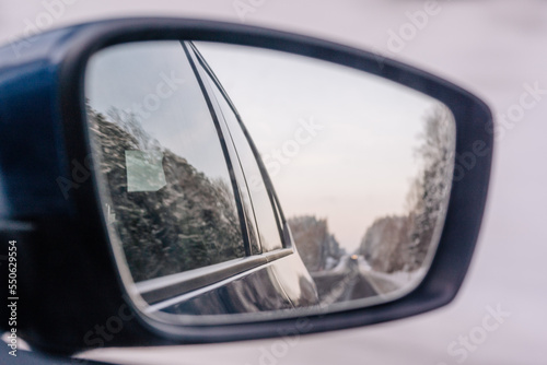 The winter road is reflected in the car s rear-view mirror