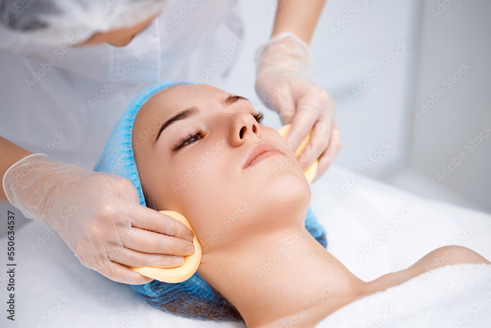 beautician cleanses skin of beautiful woman with a sponge.