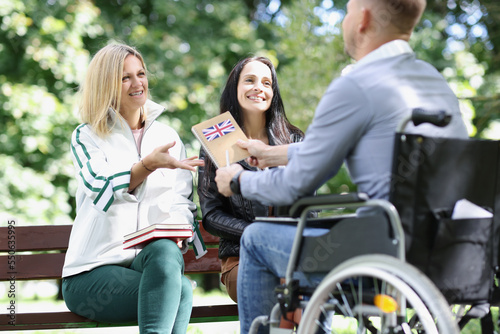 Three friends talk and study outdoors, one disabled person in wheelchair.
