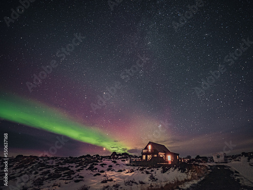 Cozy cottage in winter landscape by night with green and pink aurora borealis