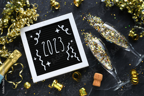 Welcoming 2023 New Year - flat lay champagne glasses bottle gold glitter confetti golden streamers photo
