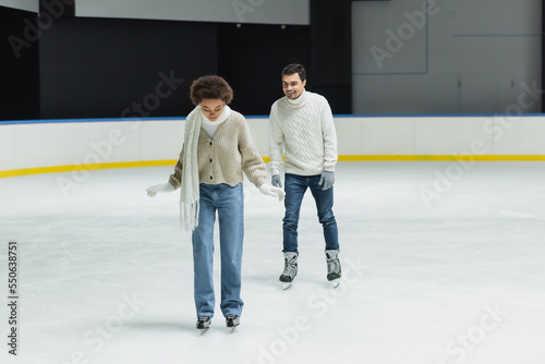 African american woman in scarf and gloves ice skating near boyfriend on rink