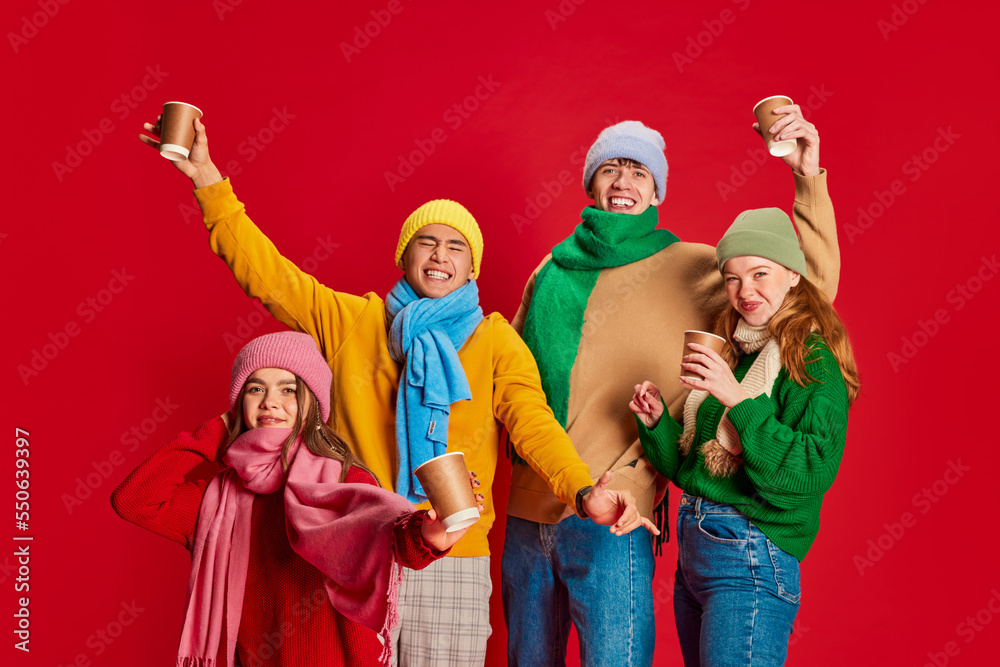 Group of young people, friends in winter clothes having fun together, posing isolated over red background. Party, festival