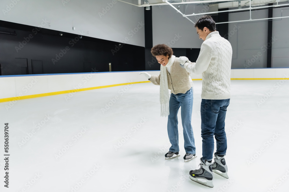 African american woman ice skating and holding hand of boyfriend on ice rink African american woman ice skating and holding hand of boyfriend on ice rink