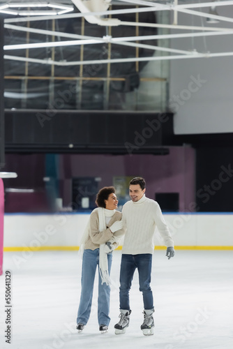 Smiling african american woman hugging boyfriend in sweater on ice rink