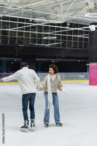 Happy african american woman ice skating with boyfriend on rink