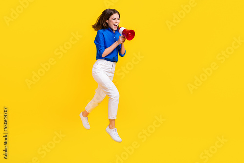 Full length photo of charming excited girl dressed blue shirt jumping high shouting toa empty space isolated yellow color background