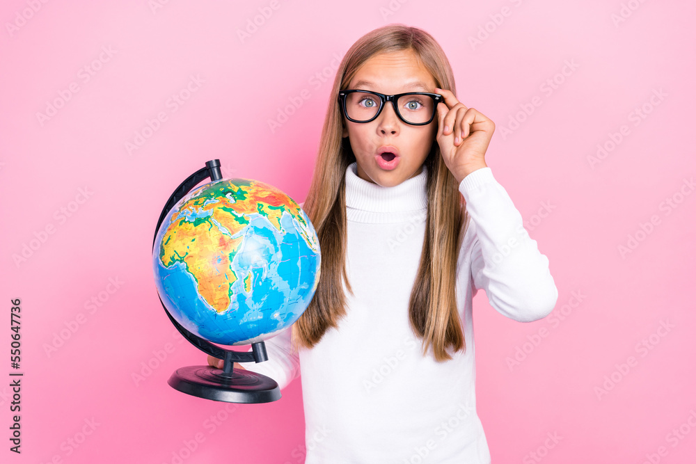 Fototapeta premium Portrait of impressed smart girl hold globe arm touch eyeglasses open mouth isolated on pink color background