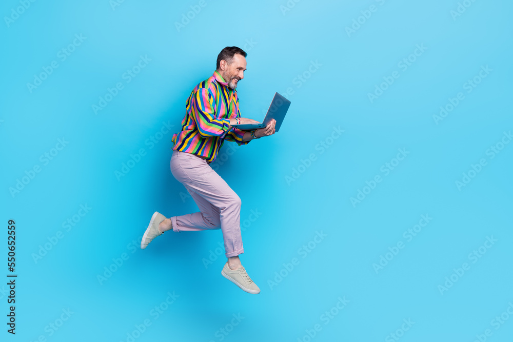 Full length photo of joyful glamour man using netbook read news feel young empty space isolated on blue color background Full length photo of joyful glamour man using netbook read news feel young empty space isolated on blue color background
