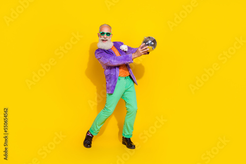 Full length photo of positive good mood guy dressed violet velvet jacket holding disco ball dancing isolated yellow color background