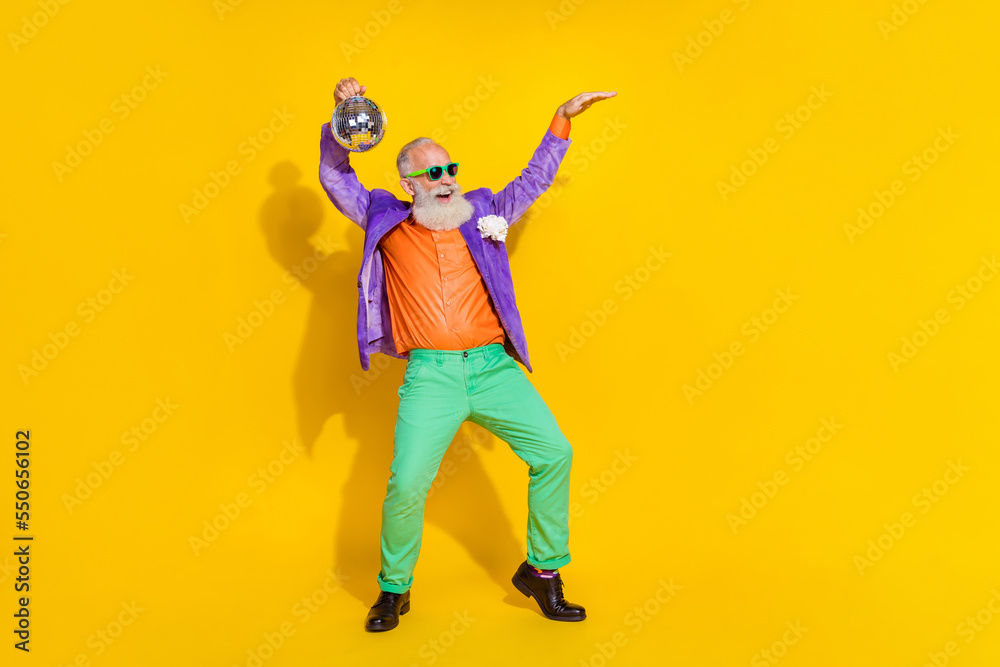 Full length photo of pretty cheerful man wear purple velvet jacket dancing rising discotheque ball empty space isolated yellow color background