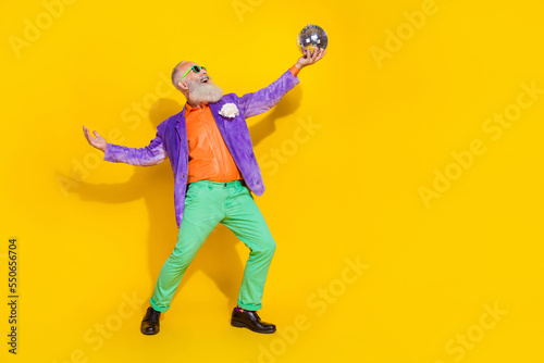 Full length photo of good mood cool guy dressed violet velvet jacket having fun rising disco ball empty space isolated yellow color background