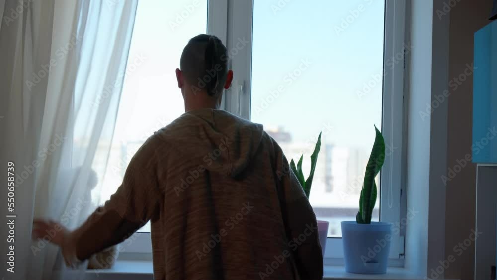 A man stands at the window of the house, covered with curtains. Selective focus A man stands at the window of the house, covered with curtains. Selective focus