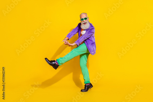 Full length photo of charming positive man wear purple velvet jacket walking dancing discotheque isolated yellow color background