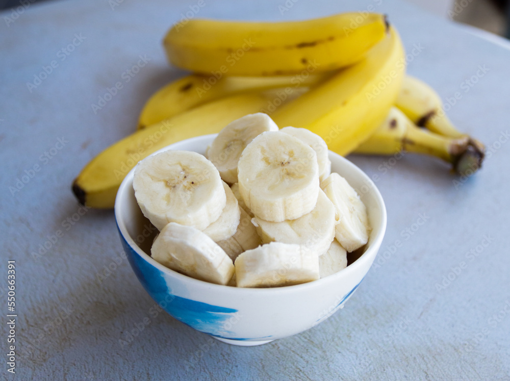 Sliced bananas in a bowl to prepare a fruit salad with whole bananas on the side. Concept of fruits and health. Sliced bananas in a bowl to prepare a fruit salad with whole bananas on the side. Concept of fruits and health.
