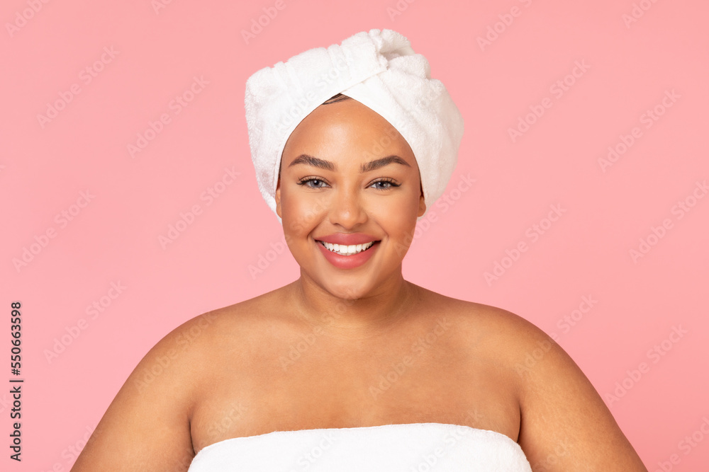 Beauty portrait of body positive black woman standing wrapped in towel over pink background and smiling at camera Beauty portrait of body positive black woman standing wrapped in towel over pink background and smiling at camera