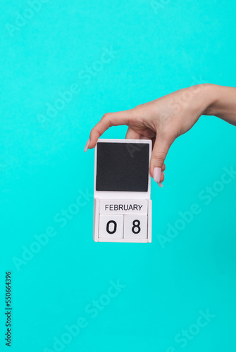 Female hand holding wooden calendar with date February 08 on blue background