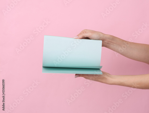 Female hands hold a notepad with blue sheets of paper on a pink pastel background.