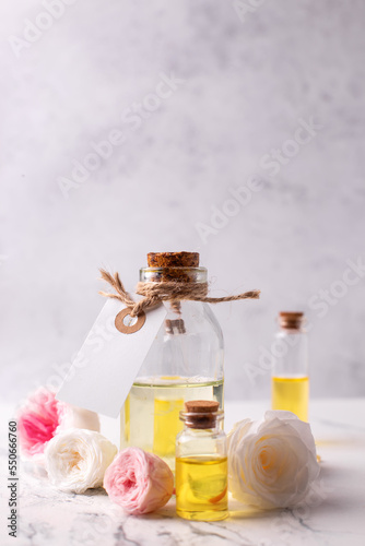 Cosmetic product. Bottles with organic  rose essential aroma oil with tag and fresh roses flowers on light  grey textured background. Selective focus. Place for text.