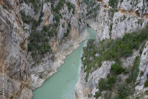Path carved into the rock of the Mont-Rebei canyon, in the Montsec saw, in Lleida, and below on the water a kayak crosses the river.