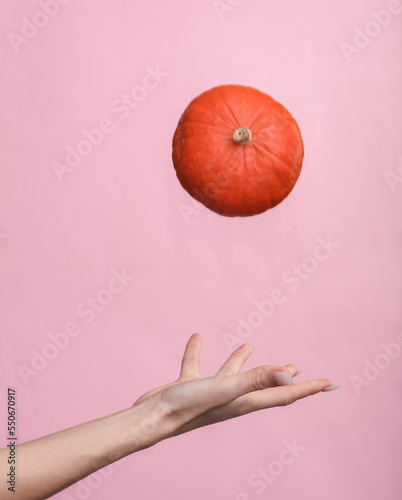 Woman's hand tossing up a pumpkin on a pink background