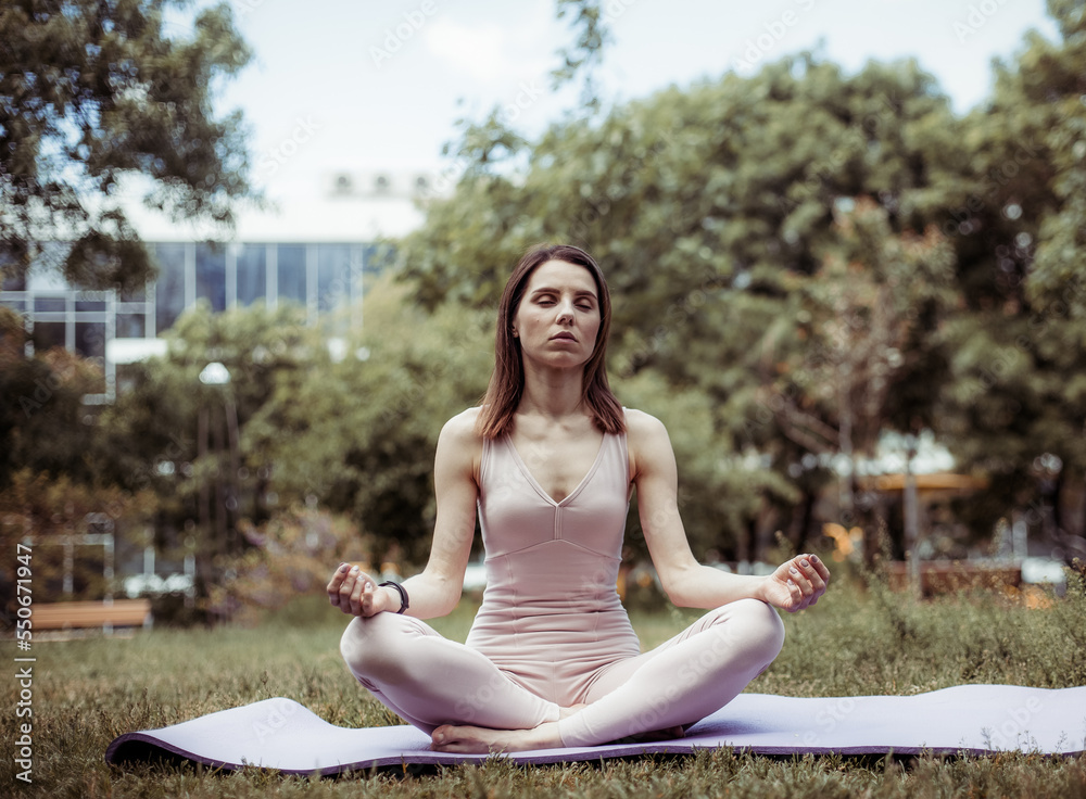 Beautiful yogi woman meditating while sitting on mat in the park