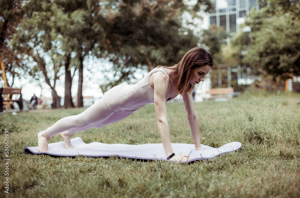 Fototapeta premium Young fit woman doing push-ups in the park. Healthy lifestyle