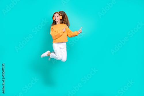 Fototapeta Naklejka Na Ścianę i Meble -  Full length photo of pretty shiny schoolgirl wear orange sweatshirt headphones jumping empty space isolated turquoise color background
